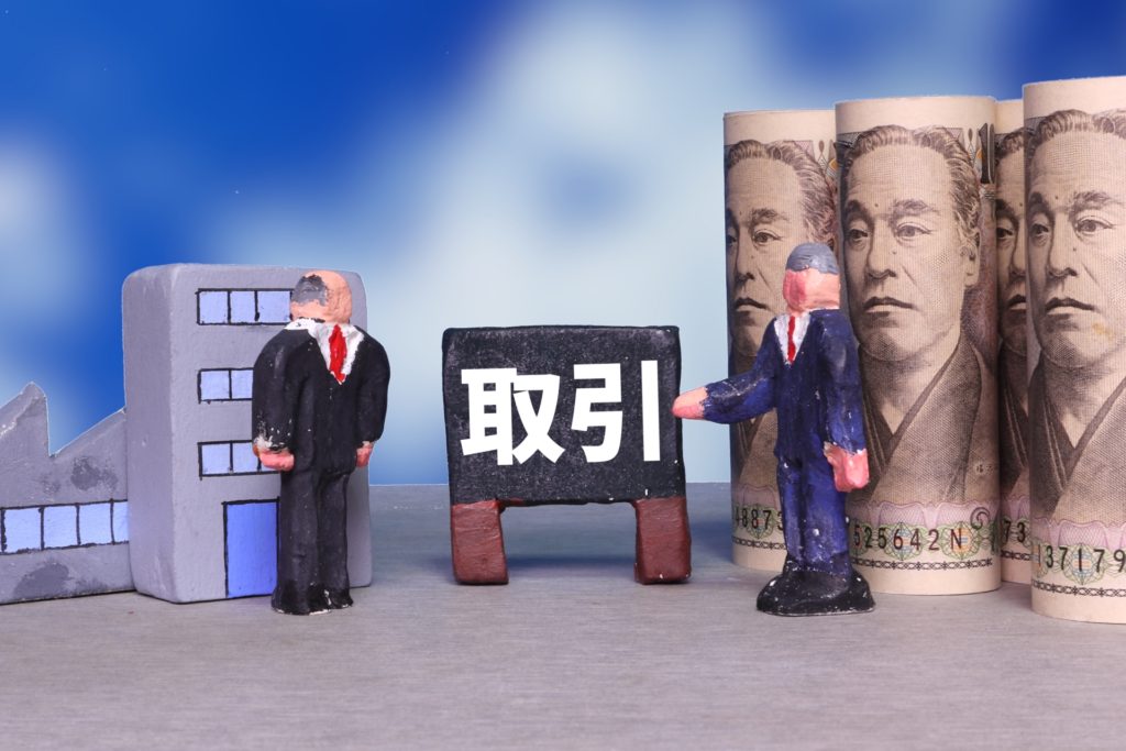 取引の看板とビジネスパーソンの人形と丸めた1万円札